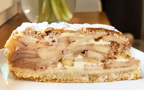 Pyszny kawałek szarlotki z warstwami jabłek i kremu, posypany cukrem pudrem. Idealna na deser, aż chce się ją piec!
