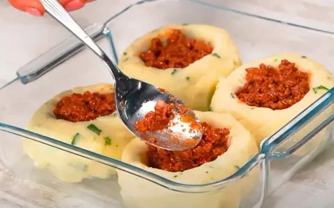 Łyżka nakłada mięsne nadzienie do wgłębień w ziemniaczanych grule, przygotowywanych w szklanym naczyniu.