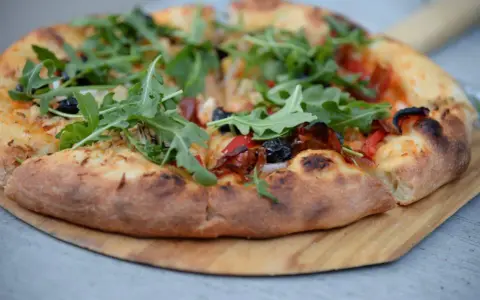Idealne ciasto na pizzę z rukolą, oliwkami i papryką, wypieczone na drewnianej desce.