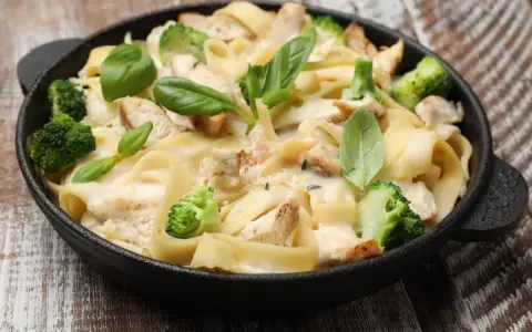 Tradycyjna potrawka z kurczaka z makaronem tagliatelle, brokułami i kremowym sosem, udekorowana świeżą bazylią.