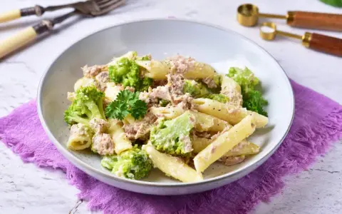 Penne z tuńczykiem i brokułami w kremowym sosie śmietanowo-serowym, udekorowane natką pietruszki.