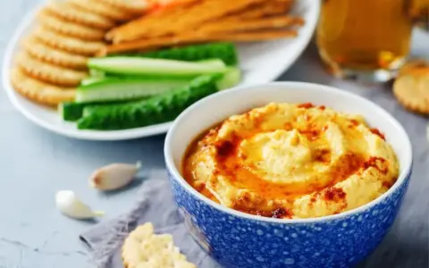 Pyszny, kremowy hummus, idealny jako sos do frytek, podany z chrupiącymi krakersami i świeżymi warzywami.
