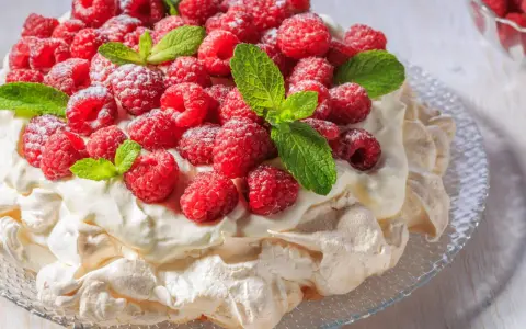 Beza Pavlova, która zawsze wychodzi, udekorowana świeżymi malinami i listkami mięty, posypana cukrem pudrem.
