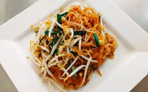 Pyszne pad thai co to? Danie z makaronem ryżowym, kiełkami fasoli mung, jajkiem i szczypiorkiem na białym talerzu.
