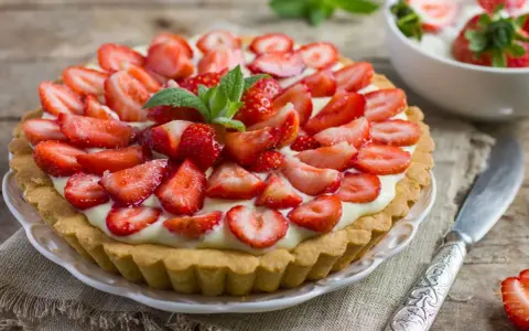 Pyszna tarta z truskawkami i kremem, ozdobiona listkami mięty. Idealna na letnie popołudnie.