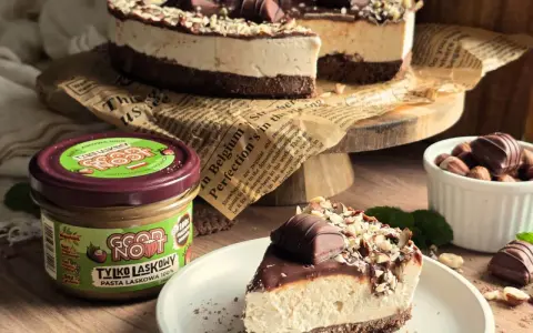 Pyszne ciasto kinder bueno z mascarpone, udekorowane orzechami i kawałkami czekolady. Obok słoik pasty z orzechów laskowych.