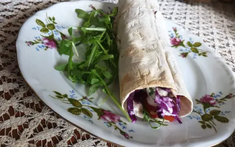 Pyszny lawasz kebab z czerwoną kapustą, pomidorem i rukolą na ozdobnym talerzu.
