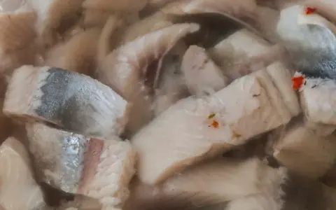Kawałki kiszonych śledzi w zalewie, z widocznymi fragmentami skórki i przyprawami.