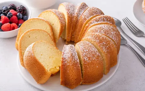 Puszysta, pokrojona wielkanocna babka posypana cukrem pudrem, obok miseczka z jagodami i malinami.