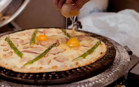 Kucharz dodaje jajko do pizzy z boczkiem i szparagami. Pyszna pizza z jajkiem w przygotowaniu.