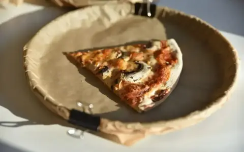 Kawałek pizzy z pieczarkami na papierowym talerzu. Zastanawiasz się, ile kalorii ma średnia pizza?