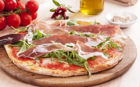 Pyszna pizza prosciutto z rukolą, pomidorami i oliwą z oliwek. Idealna na włoską ucztę.