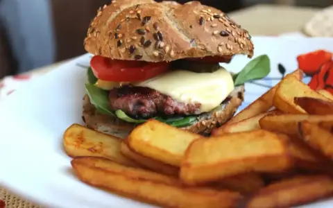 Pyszne, prawdziwe burgery przepis na domowy obiad. Soczysty kotlet, ser, warzywa i chrupiące frytki na talerzu.