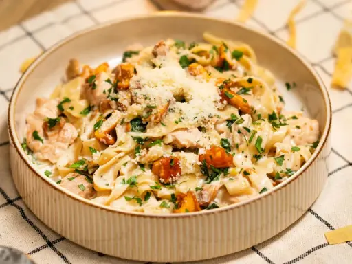 Pyszny makaron w sosie kurkowym z kawałkami kurczaka i posypany parmezanem.
