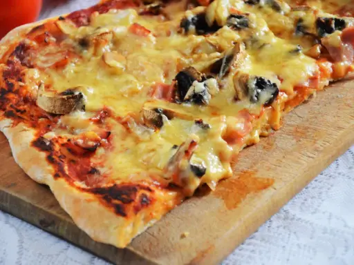 Pyszna pizza capriciosa z pieczarkami i szynką, roztopiony ser ciągnie się na chrupiącym cieście.