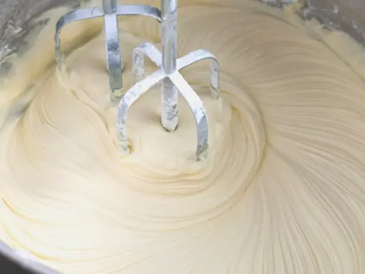 Mieszadła miksera zagłębiają się w puszysty krem z mascarpone i białej czekolady, tworząc faliste wzory.