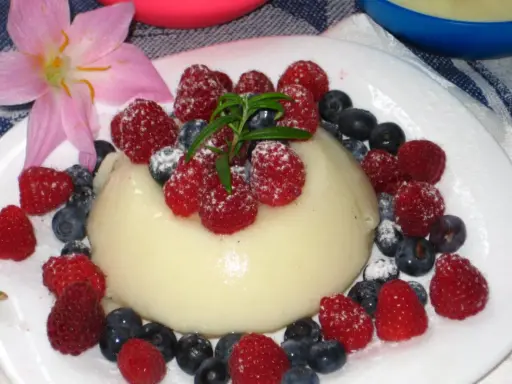 Panna cotta z malinami i borówkami, posypana cukrem pudrem. Idealny deser, który można zrobić według prostego legumina przepisu.