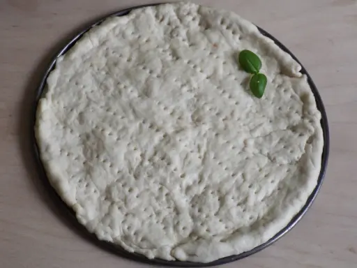 Gotowy do pieczenia, okrągły spód do pizzy z dziurkami, ozdobiony listkiem bazylii. Idealny szybki przepis na ciasto do pizzy.