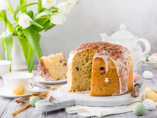 Pyszna babka włoska z lukrem i czekoladową posypką, udekorowana na Wielkanoc z tulipanami i kolorowymi jajeczkami.