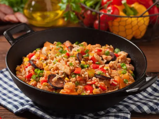 Pyszne jambalaya z kurczakiem, kiełbasą, kukurydzą i papryką w czarnej patelni.