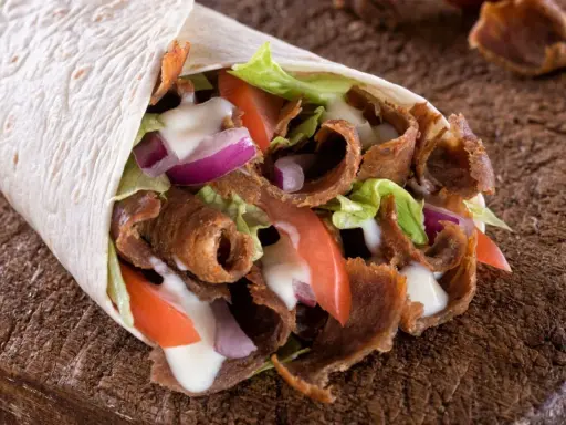 Pyszny, domowy kebab zawinięty w tortillę z soczystym mięsem, chrupiącą sałatą, pomidorami i cebulą, polany sosem.