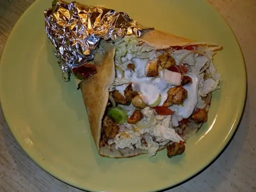 Pyszny kebab w tortilli z kurczakiem, warzywami i sosem na zielonym talerzu.