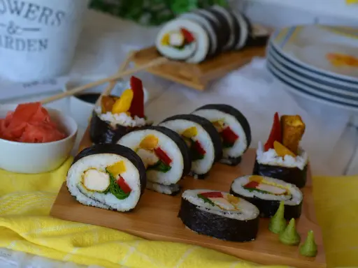 Pyszne sushi z kurczakiem, papryką i mango. Podane na desce z dodatkami: marynowanym imbirem i wasabi.