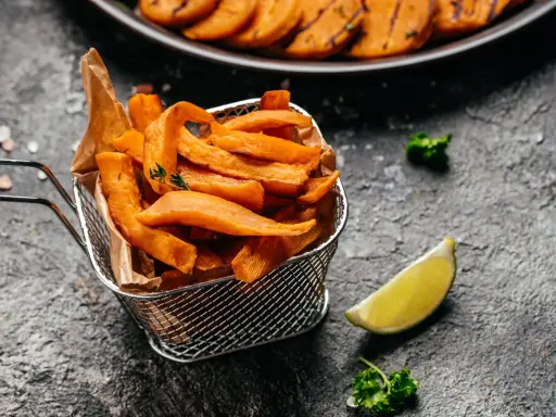 Chrupiące frytki z batatów z frytkownicy airfryer, podane w metalowym koszyku, z limonką i natką pietruszki.