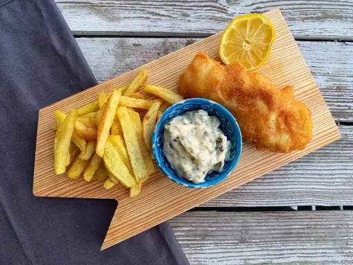 Chrupiące fish and chips z cytryną i sosem tatarskim na drewnianej desce.
