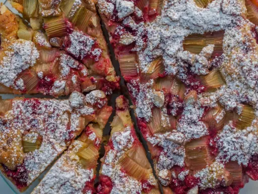 Pyszne ciasto z rabarbarem i malinami, posypane cukrem pudrem. Idealny przepis na letnie popołudnie.