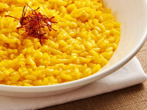 Aksamitne risotto alla milanese, złociste od szafranu, podane w białej misce, ozdobione nitkami szafranu.