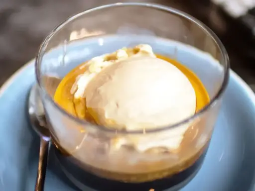 Pyszne affogato: gałka lodów waniliowych w gorącym espresso, podana w szklance na niebieskim talerzyku.