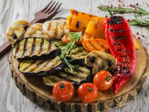 Pyszne warzywa na grilla: grillowany bakłażan, papryka, pieczarki, pomidorki i czerwona papryka, udekorowane rozmarynem.