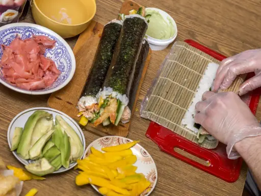 Przygotowanie uramaki: ryż, awokado, mango, krewetki i marynowany imbir czekają na zwinięcie w pyszne rolki sushi.