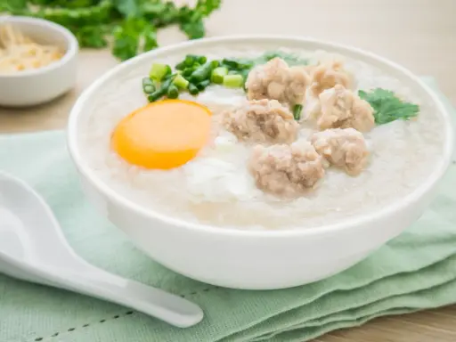 Miseczka aromatycznego congee z mięsnymi klopsikami, jajkiem i szczypiorkiem.