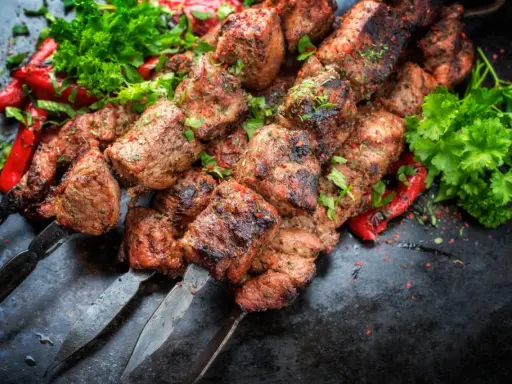 Soczyste kawałki mięsa na szpadach, przypominające kofta kebab, podane z pieczoną papryką i świeżą natką pietruszki.