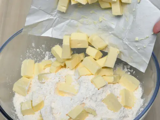 Kawałki zimnego masła dodawane do mąki w misce, kluczowy krok w sprawdzonym przepisie na kruche ciasto.