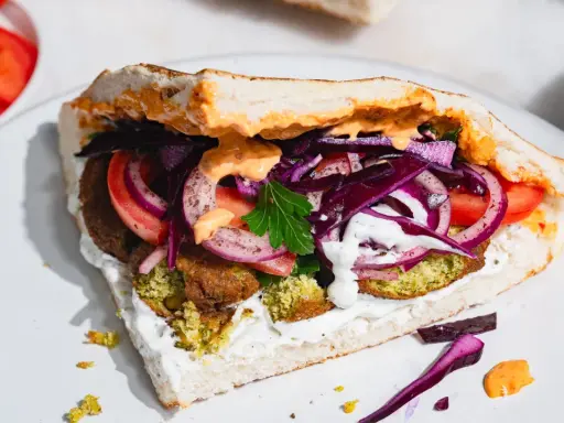 Pyszny falafel kebab w bułce z pomidorami, czerwoną cebulą, kapustą i sosami.