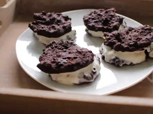 Cztery domowe ciastka Oreo z kremowym nadzieniem, ułożone na białym talerzu.