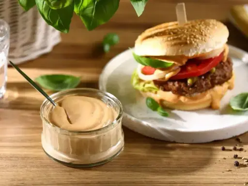 Pyszny sos do burgera w słoiczku, obok apetyczny burger z dodatkami. Idealny duet na letni wieczór.