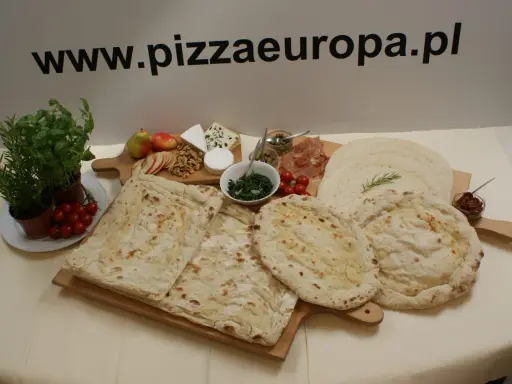 Gotowe ciasto na pizzę, świeże zioła, pomidorki, ser i inne dodatki na drewnianych deskach. Idealne na domowe wypieki.