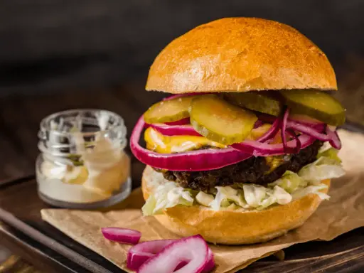 Soczysty burger z ogórkiem, czerwoną cebulą i majonezem, idealny do przygotowania, jak smażyć burgera na patelni.