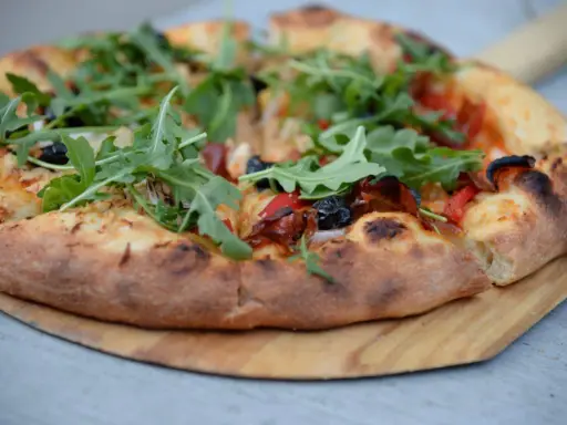 Idealne ciasto na pizzę z rukolą, oliwkami i papryką, wypieczone na drewnianej desce.