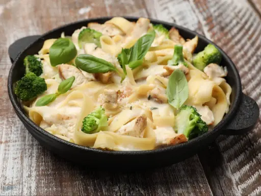Tradycyjna potrawka z kurczaka z makaronem tagliatelle, brokułami i kremowym sosem, udekorowana świeżą bazylią.