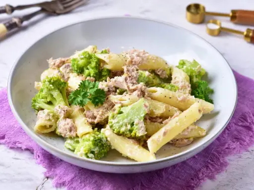 Penne z tuńczykiem i brokułami w kremowym sosie śmietanowo-serowym, udekorowane natką pietruszki.