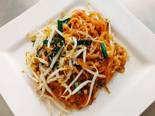 Pyszne pad thai co to? Danie z makaronem ryżowym, kiełkami fasoli mung, jajkiem i szczypiorkiem na białym talerzu.