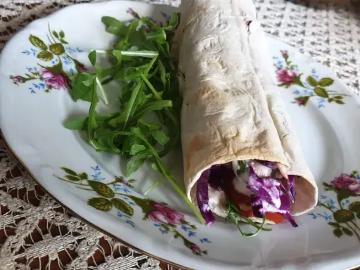 Pyszny lawasz kebab z czerwoną kapustą, pomidorem i rukolą na ozdobnym talerzu.