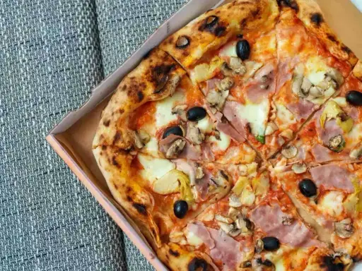 Pizza capricciosa z szynką, pieczarkami, karczochami i czarnymi oliwkami, w pudełku.