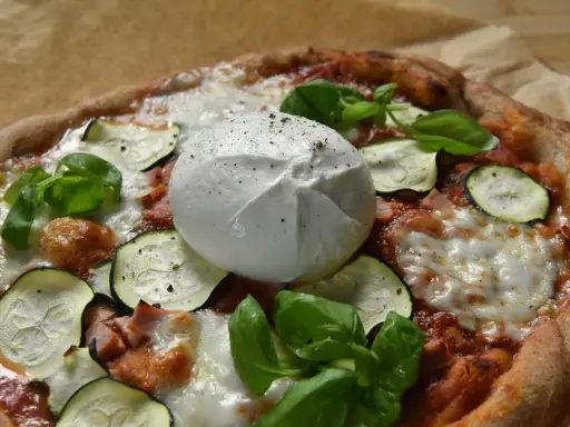 Pyszna pizza z burrata, cukinią i bazylią, posypana świeżo mielonym pieprzem.