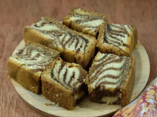 Puszyste ciasto zebra przepis. Pokrojone kawałki ciasta z charakterystycznym wzorem zebry ułożone na drewnianej desce.
